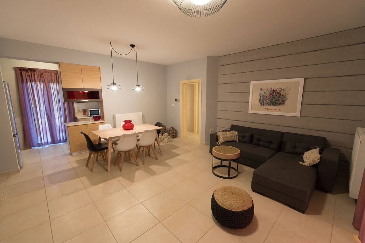 A modern living room with a grey sofa, a round coffee table, and a dining area with a white table and chairs.