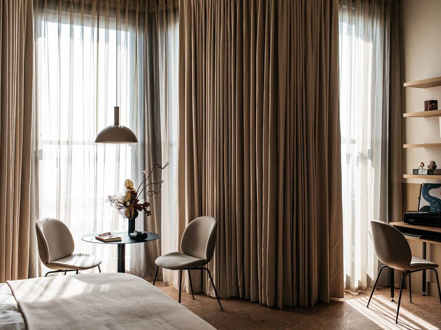 A hotel room with a bed, two chairs, a small table with a vase, and a desk with shelves.