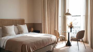 Une chambre d’hôtel avec un lit, une petite table et des chaises, et une vue sur l’extérieur grâce à de grandes fenêtres.
