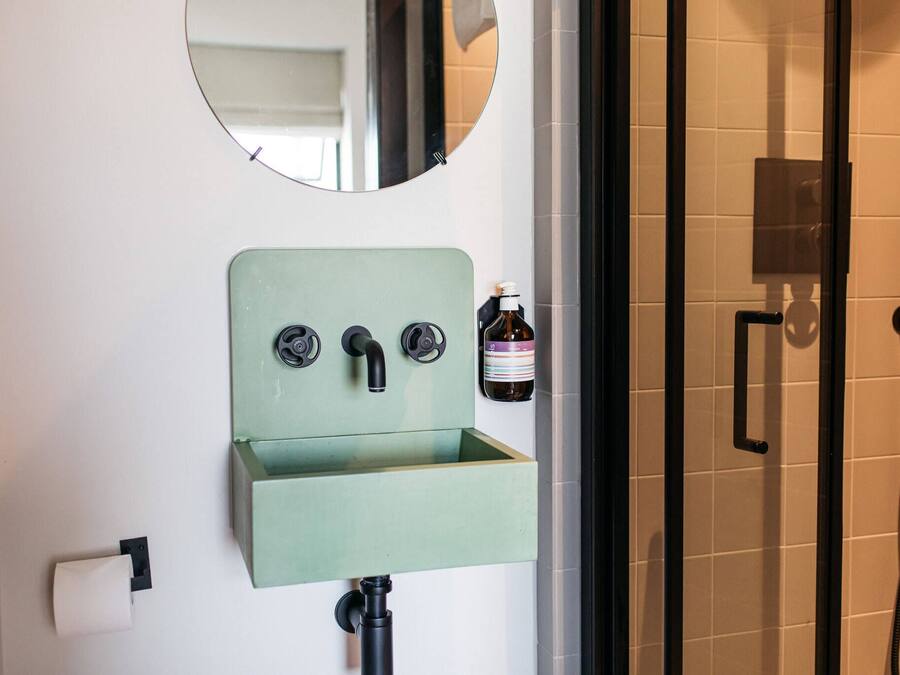Een badkamer met een groen wastafel, een spiegel, een toiletrolhouder en een douche.