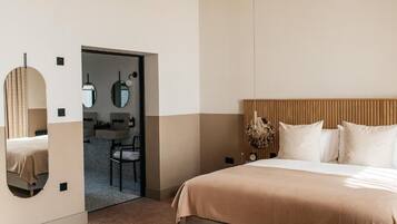 A modern hotel room with a large bed, a wooden headboard, a mirror, and a small desk with a chair.