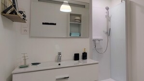 Et moderne badeværelse med et hvidt skab, et spejl, en bruseniche og en hængende lampe.
