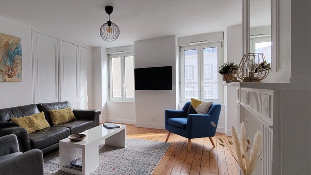 En moderne stue med en sort lædersofa, en blå lænestol, et hvidt sofabord og et fladskærms-tv ophængt på væggen.