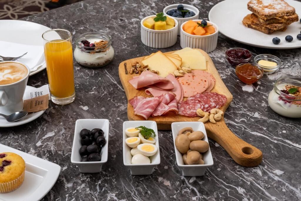 A breakfast spread with various cheeses, meats, fruits, and eggs on a marble table.