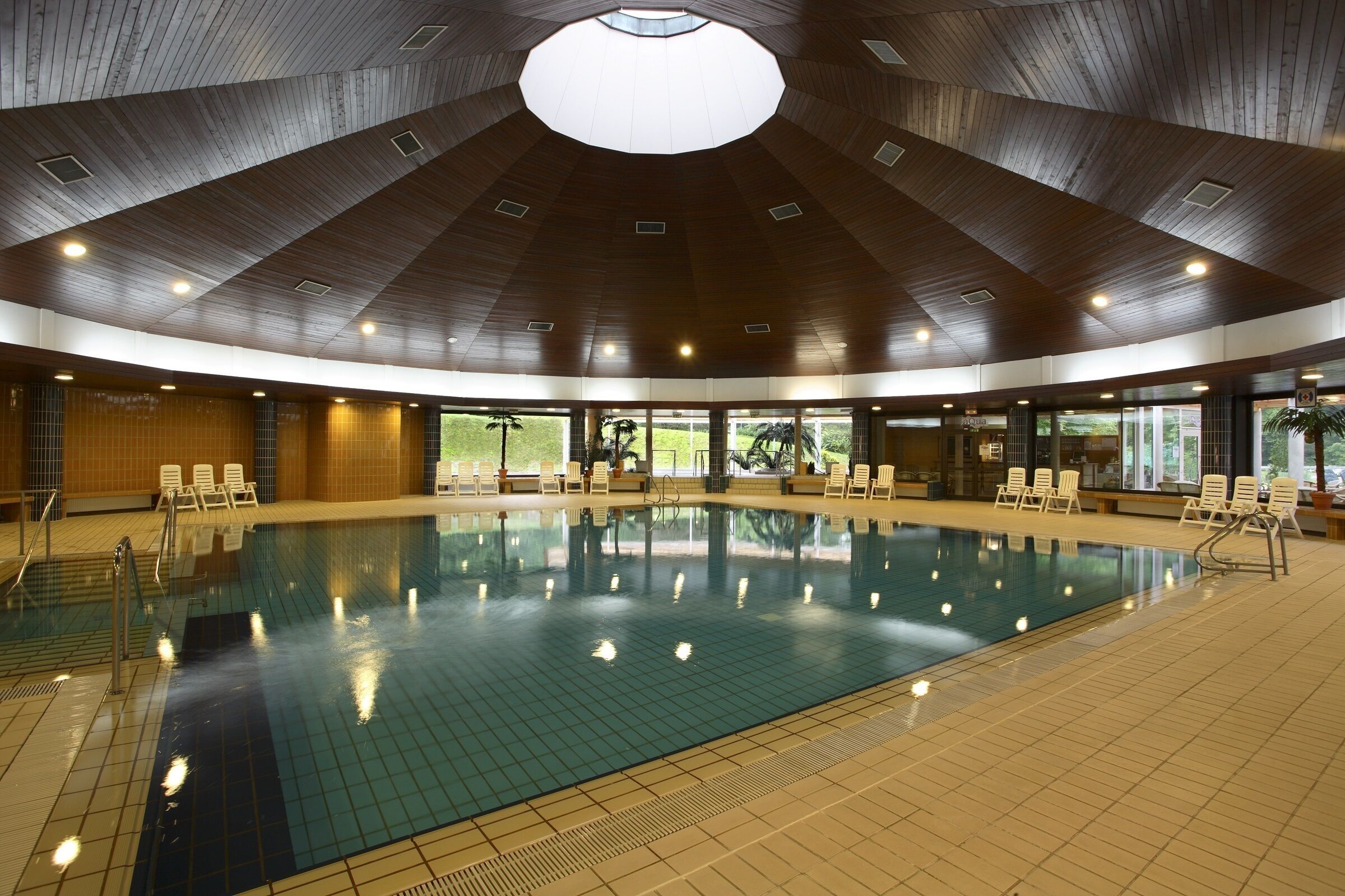 A large indoor swimming pool with a wooden ceiling and multiple windows.
