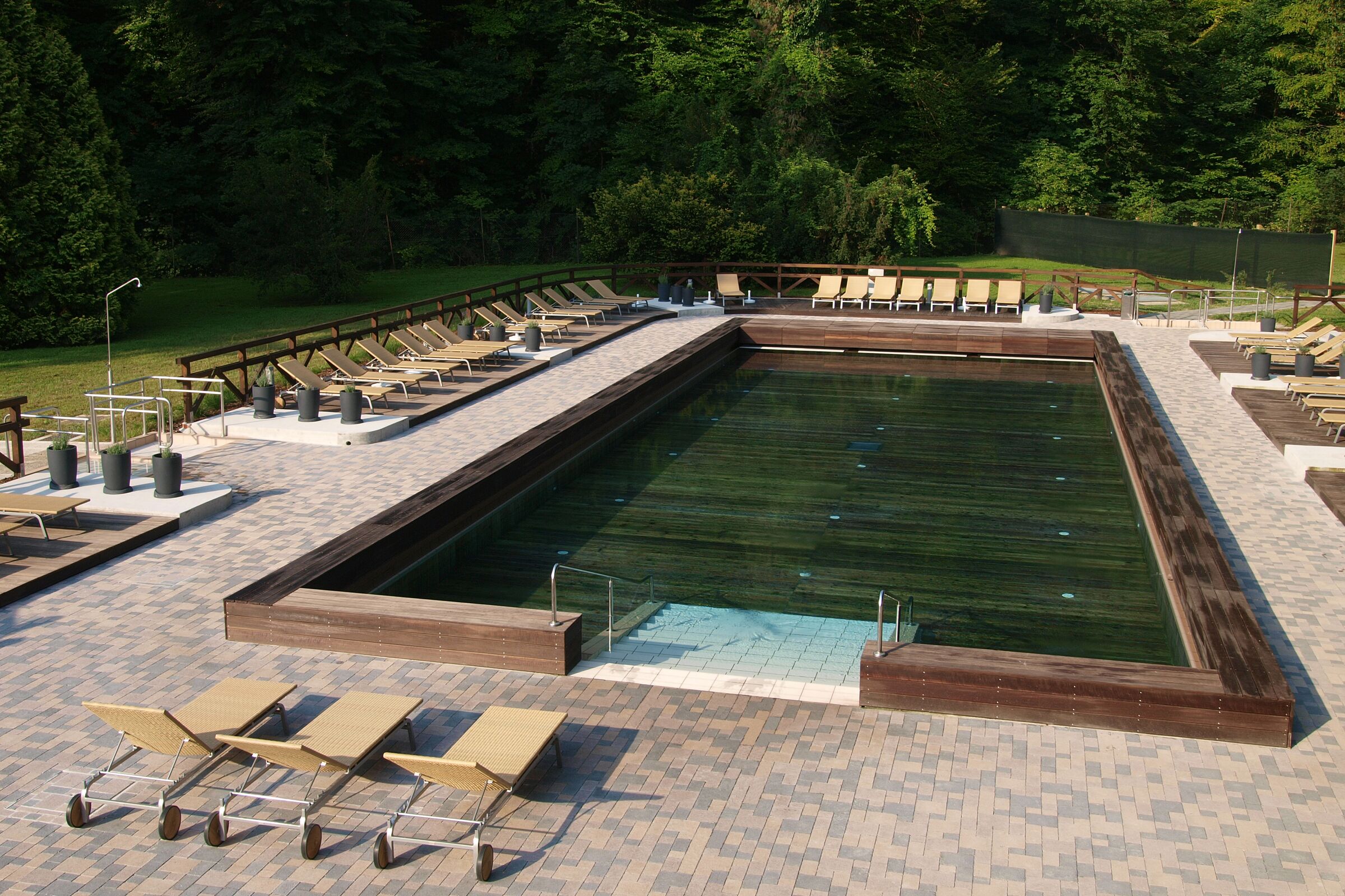 A rectangular pool with a wooden deck, surrounded by lounge chairs and potted plants.