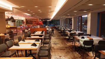 A spacious restaurant with multiple tables and chairs, a patterned carpet, and large windows offering a view.