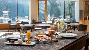 Um buffet de café da manhã com diversas opções de comida e bebidas em uma bancada de mármore em um ambiente bem iluminado e com grandes janelas.