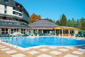 A swimming pool with a tiled deck, a covered seating area, and a building with multiple balconies. - Hotel Toplice - Terme Krka (Smarjeske Toplice)