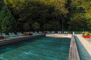 A swimming pool with lounge chairs and a wooden deck, surrounded by dense forest. - Hotel Toplice - Terme Krka (Smarjeske Toplice)