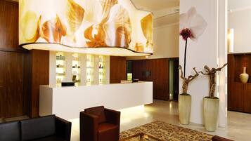A modern lobby with a reception desk, seating area, and decorative elements like a large orchid and two potted plants.