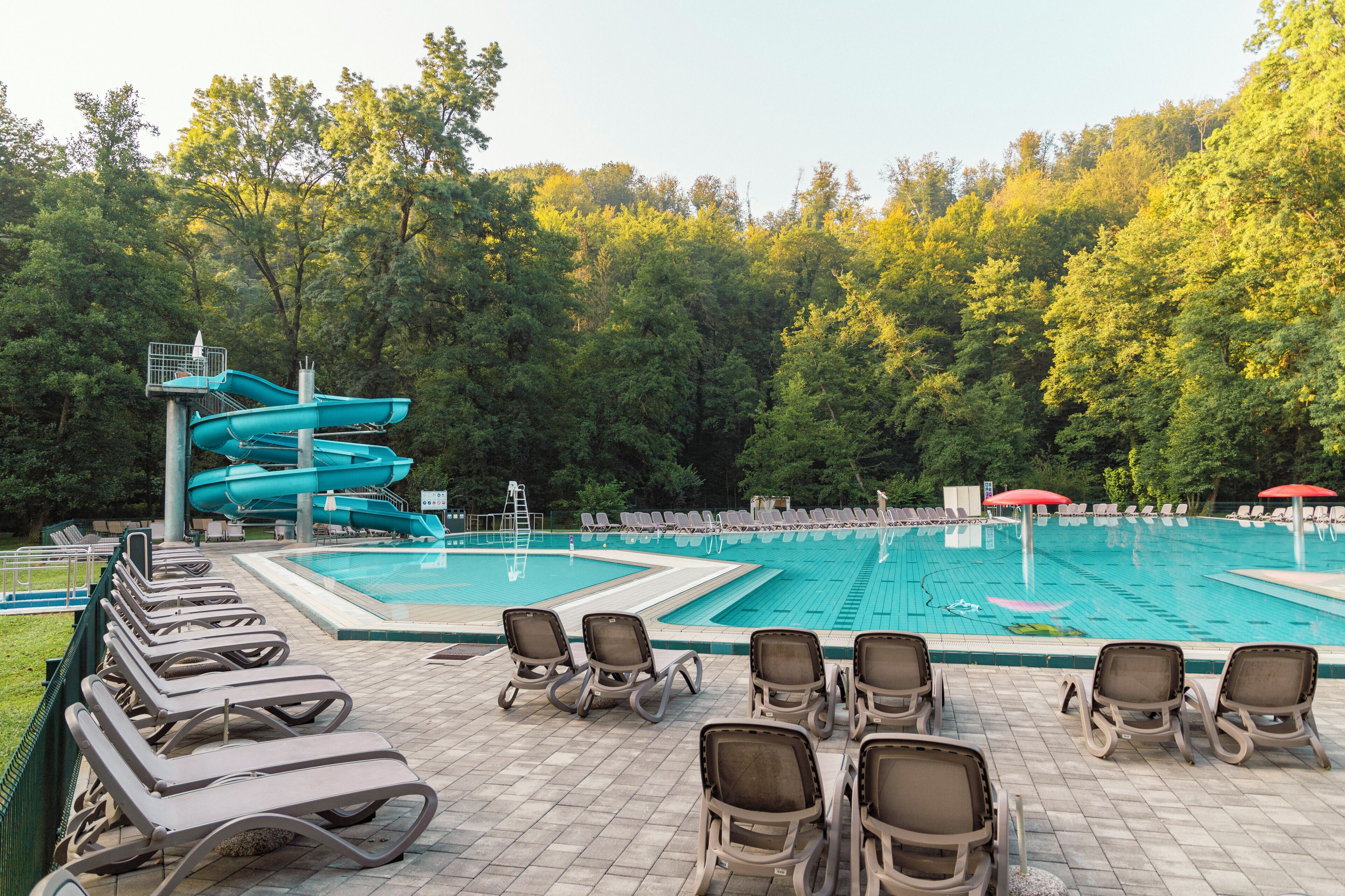 A swimming pool with a water slide, lounge chairs, and a forested backdrop.