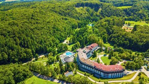 Vista aérea de um hotel com piscina, rodeado por uma floresta densa.