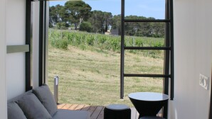 A compact room with a sofa, a small round table, and a bench. A skylight provides natural light, and the room has a view of a grassy area with trees. - Eco-lodges Lodges in Move - Domaine de Brau (Villemoustaussou)