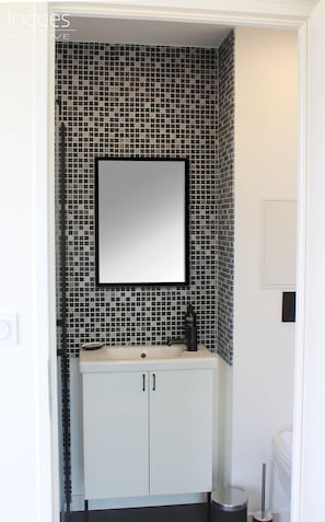 Et badeværelse med flisebeklædt bagpanel, et spejl, en vask og et toilet.