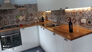A modern kitchen with white cabinets, a gas stove, a built-in oven, a stainless steel sink, and a patterned backsplash. - MaGi Holiday Home (Stintino)