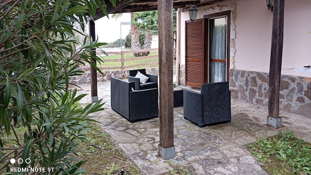 An outdoor seating area with wicker furniture under a wooden pergola, stone flooring, and a stone wall. - MaGi Holiday Home (Stintino)