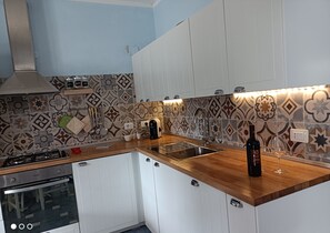 A modern kitchen with white cabinets, a gas stove, a built-in oven, a stainless steel sink, and a patterned backsplash. - MaGi Holiday Home (Stintino)