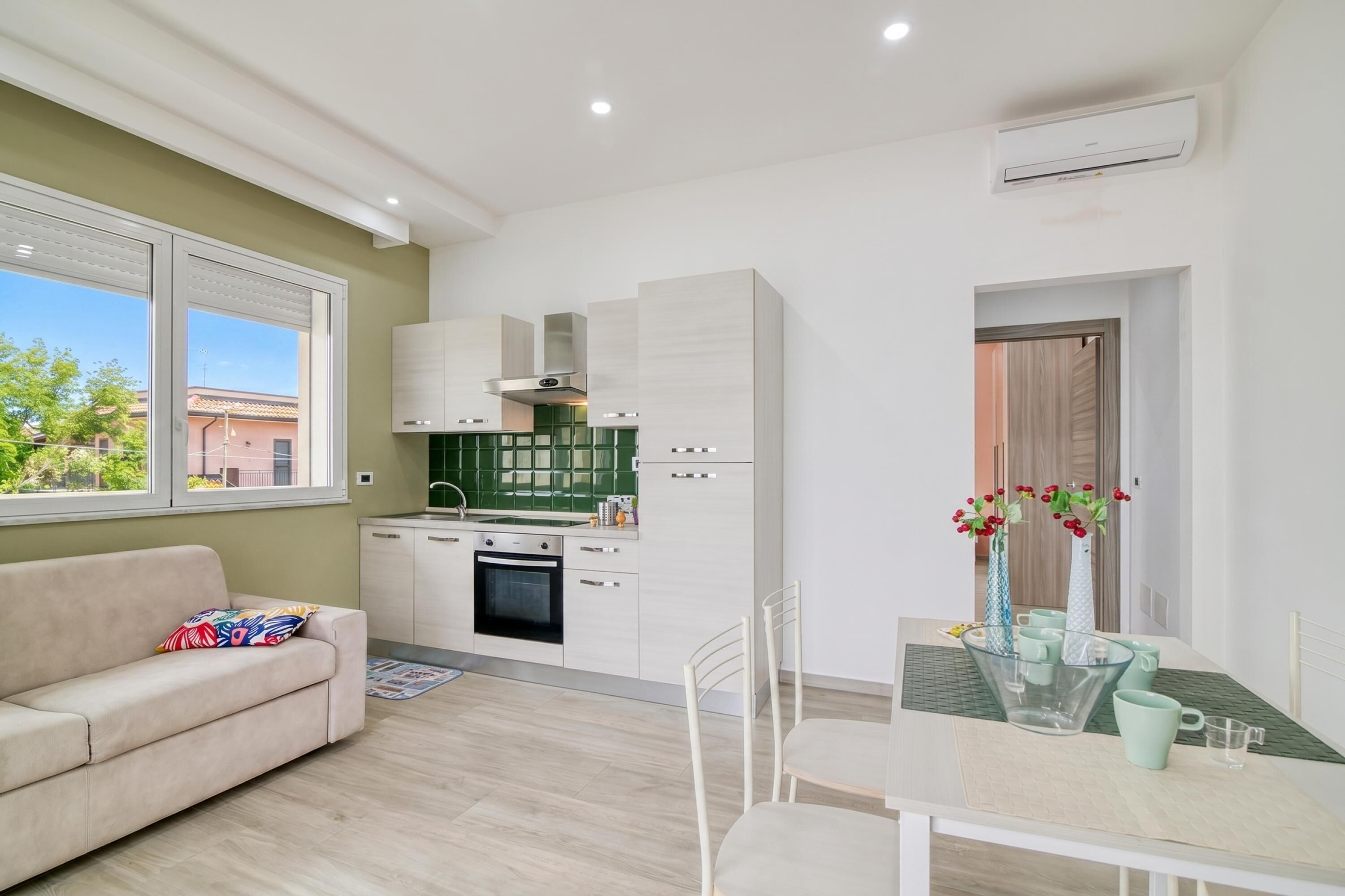 A modern kitchen with white cabinets, a green backsplash, and a dining area with a table and chairs.