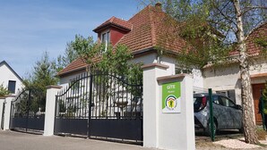 Un lotissement résidentiel fermé, avec un bâtiment blanc, un toit recouvert de tuiles rouges et un panneau indiquant qu’il fait partie du réseau GITE Alsace.