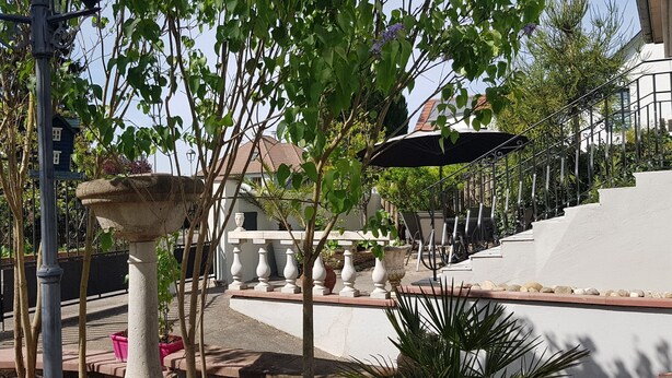 Une cour intérieure agrémentée d’une fontaine en pierre, de plantes en pot et d’un escalier menant à un bâtiment.