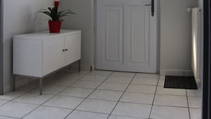 Un couloir avec une porte blanche, une plante en pot, un petit miroir et un thermostat fixé au mur.
