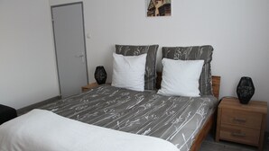 Un lit double recouvert d’une couvre-lit à motifs floraux gris et blancs, deux tables de chevet avec des vases noirs et une table de nuit en bois dotée d’un tiroir.