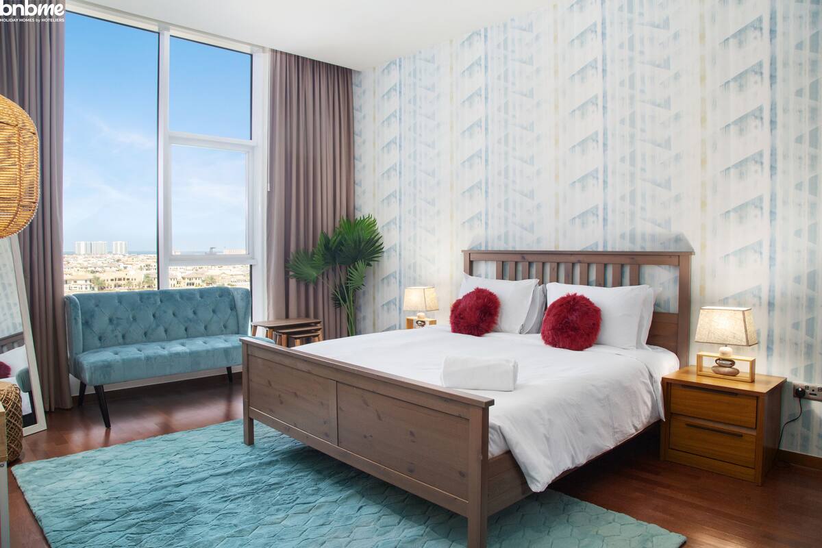 Un dormitorio con una cama grande, un sofá azul y vistas de la ciudad, además de un paisaje urbano a través de la ventana.
