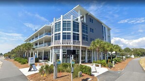 A modern hotel with a curved facade, multiple balconies, and a sign indicating a surfing destination. - Family Ties- Gulf Front- Perfect Panoramic Gulf Views- Private Pool- 4 Bikes (Santa Rosa Beach)