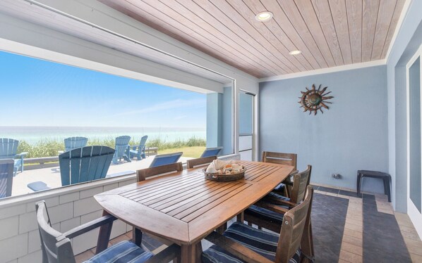 Una mesa de madera con sillas, un adorno de sol en la pared y vistas al océano.