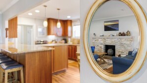 A modern kitchen with wooden cabinets and a central island, a living room with a fireplace and blue furniture, and a round mirror reflecting the living room. - Family Ties- Gulf Front- Perfect Panoramic Gulf Views- Private Pool- 4 Bikes (Santa Rosa Beach)