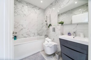 A bathroom with a marble wall, a bathtub, a toilet, a sink, and a mirror.