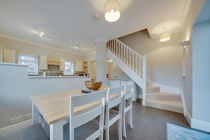 A modern kitchen with white cabinetry, a dining area with a wooden table and white chairs, and a staircase leading to an upper level.