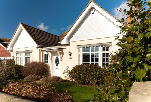 A white two-story house with a gabled roof, a front door with a decorative glass panel, and a small porch.