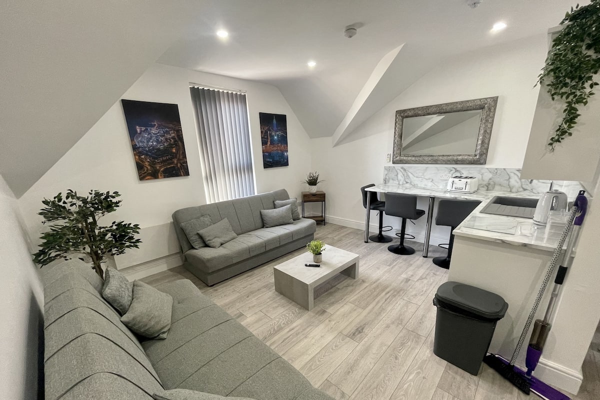 Una sala de estar moderna con un sofá seccional gris, una mesa de centro y un comedor con encimera de mármol blanco y sillas negras.