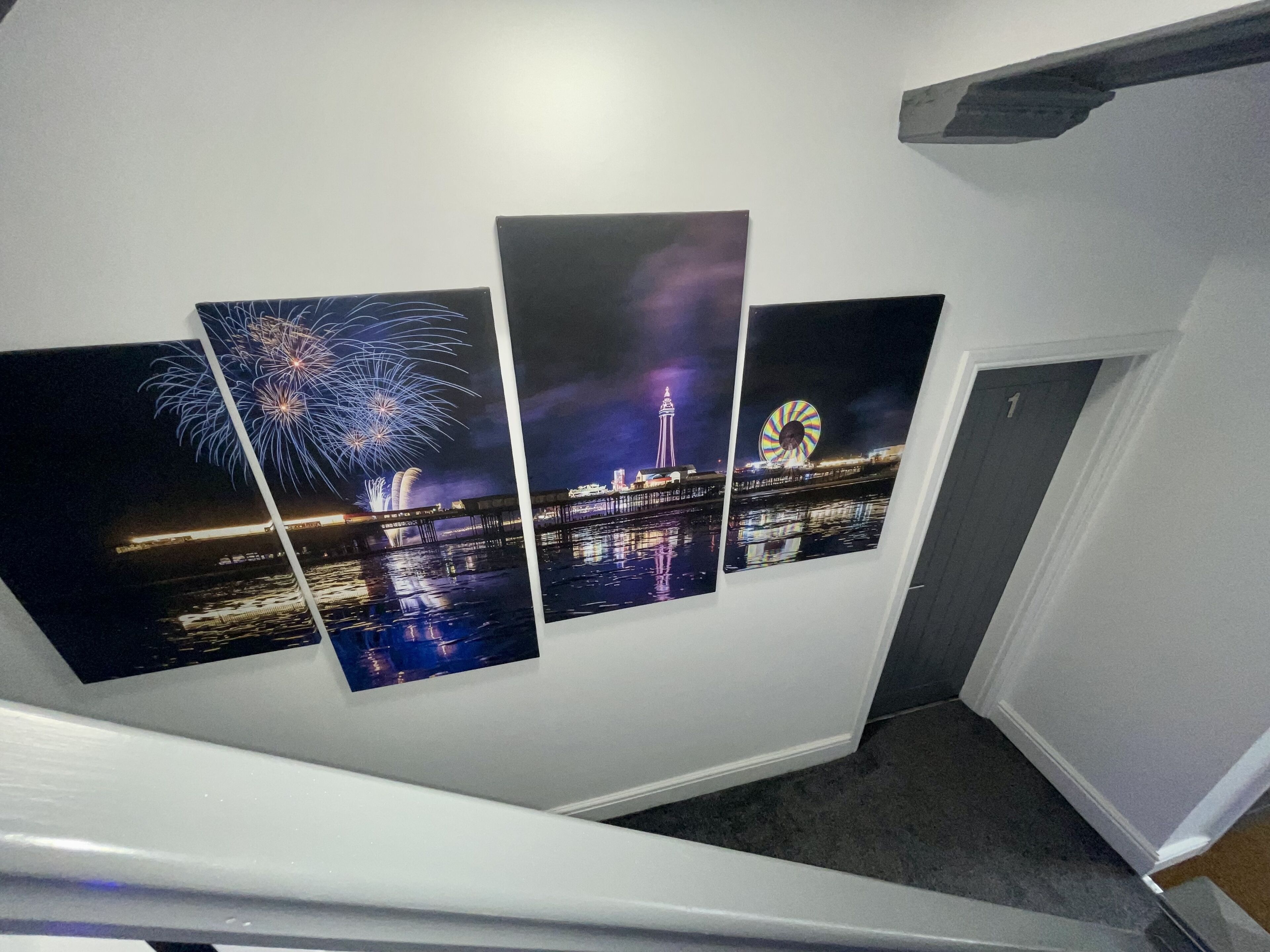 A staircase with three framed artworks depicting fireworks, a Ferris wheel, and a cityscape at night.