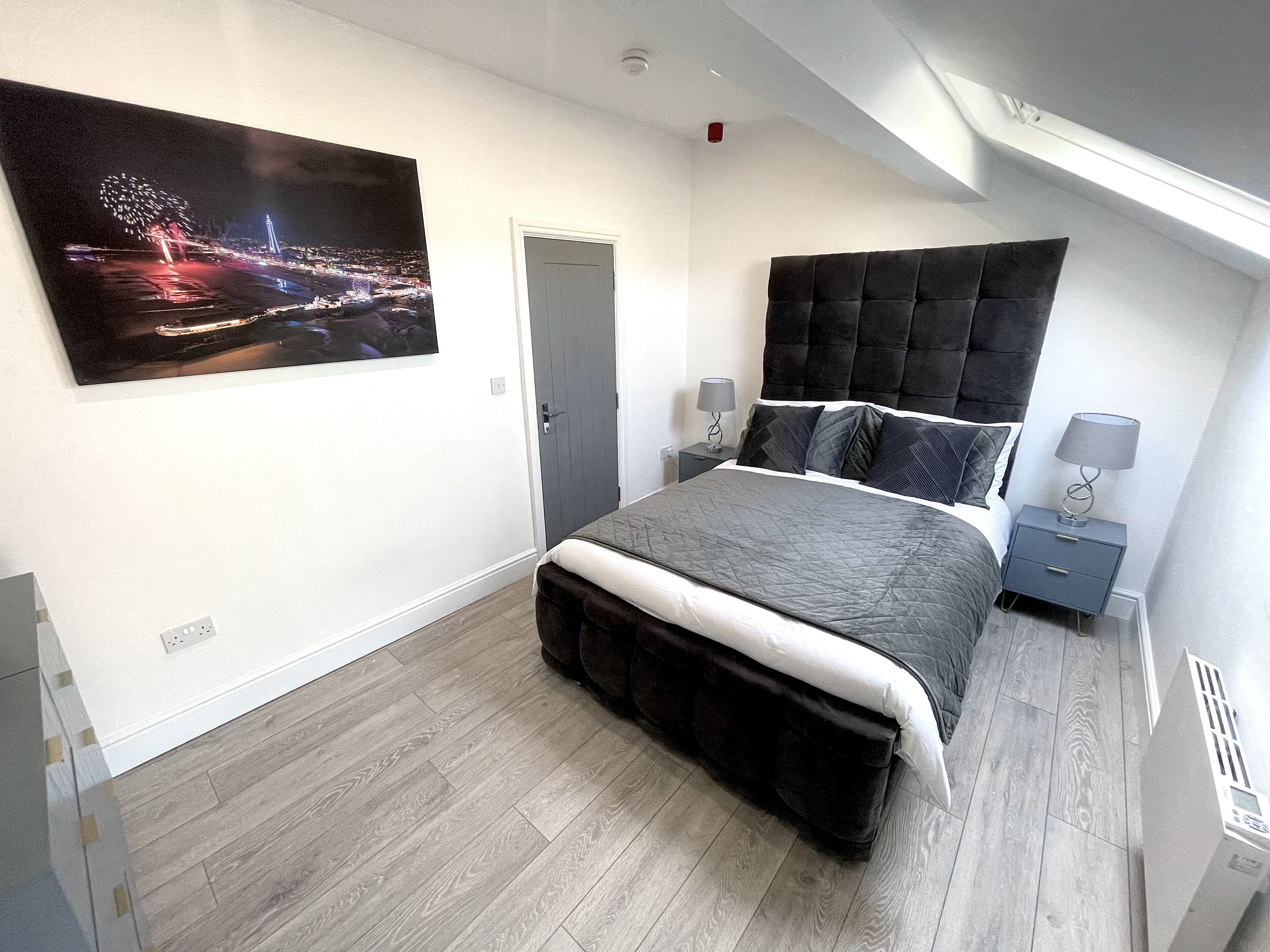 A modern bedroom with a large bed, a nightstand, a wall-mounted TV, and a door.