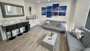A modern living room with a grey sofa, a coffee table, and a kitchen area with a marble countertop. - Osborne Luxury Hot Tub and Jacuzzi Suites (Blackpool)