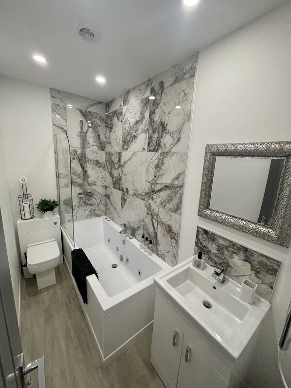 Un baño moderno con pared de mármol, bañera, lavamanos e inodoro.