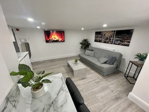 Un salon moderne avec un canapé gris, une table basse et une cheminée. On peut voir une plante sur la table basse et une autre sur le sol.