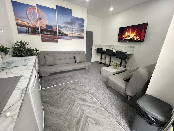 Un salon moderne avec un canapé, une table basse, un téléviseur et une cheminée. Trois tableaux sont accrochés au mur, et il y a une plante en pot.
