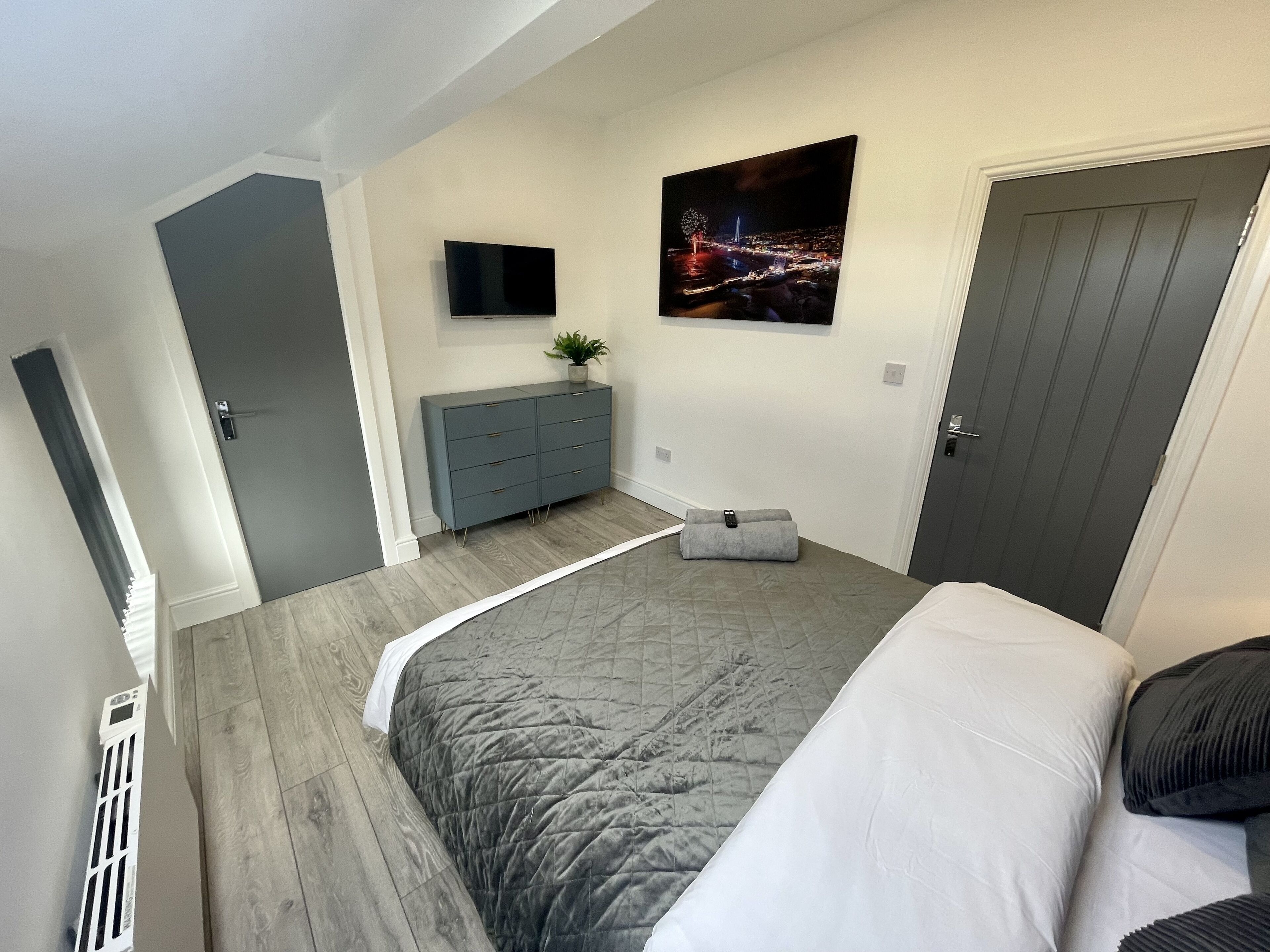 A bedroom with a bed, a dresser, a TV, and a painting.