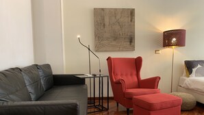 A modern living room with a black leather sofa, a red armchair, a small table, a floor lamp, and a bed with a white comforter. - SmooRoomS Trastevere (Rome)
