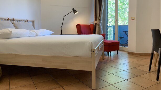 A bedroom with a bed, a desk, a chair, and a balcony with a view. - SmooRoomS Trastevere (Rome)