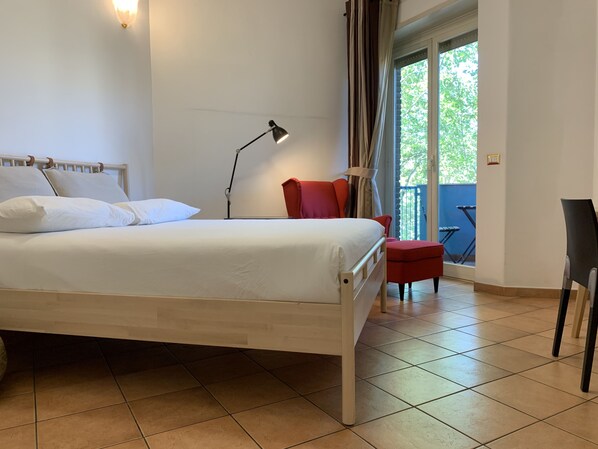 A bedroom with a bed, a desk, a chair, and a balcony with a view. - SmooRoomS Trastevere (Rome)