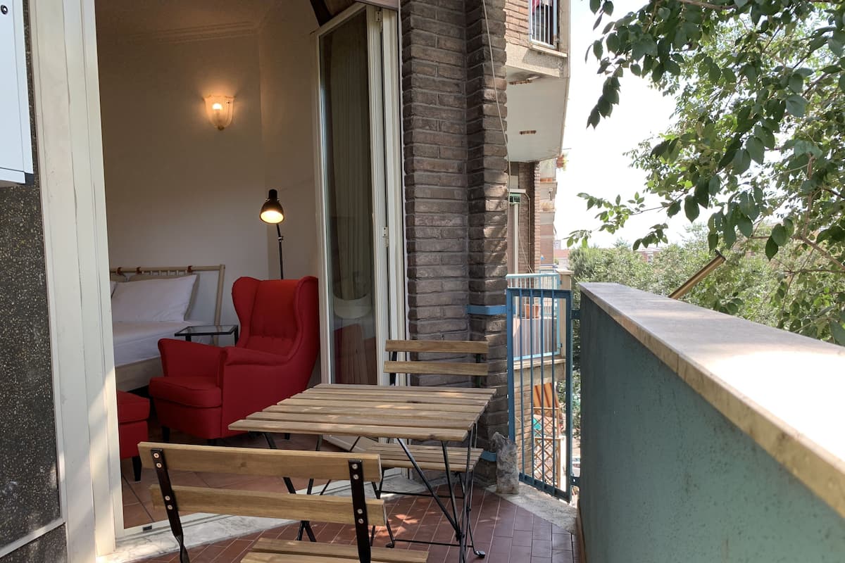 A balcony with a wooden table and chairs, a red chair, and a lamp.