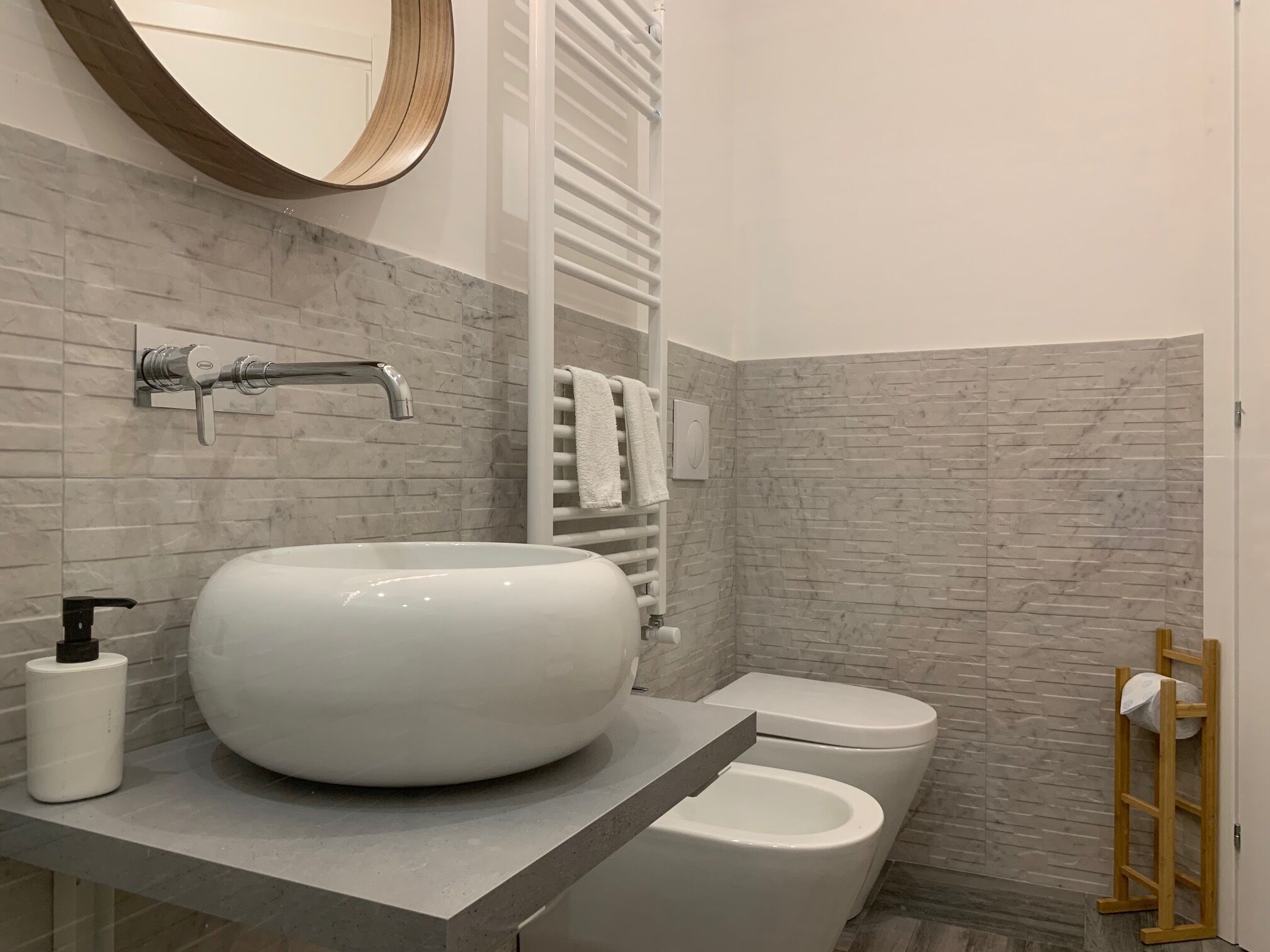A bathroom with a round white sink, a toilet, and a towel rack.