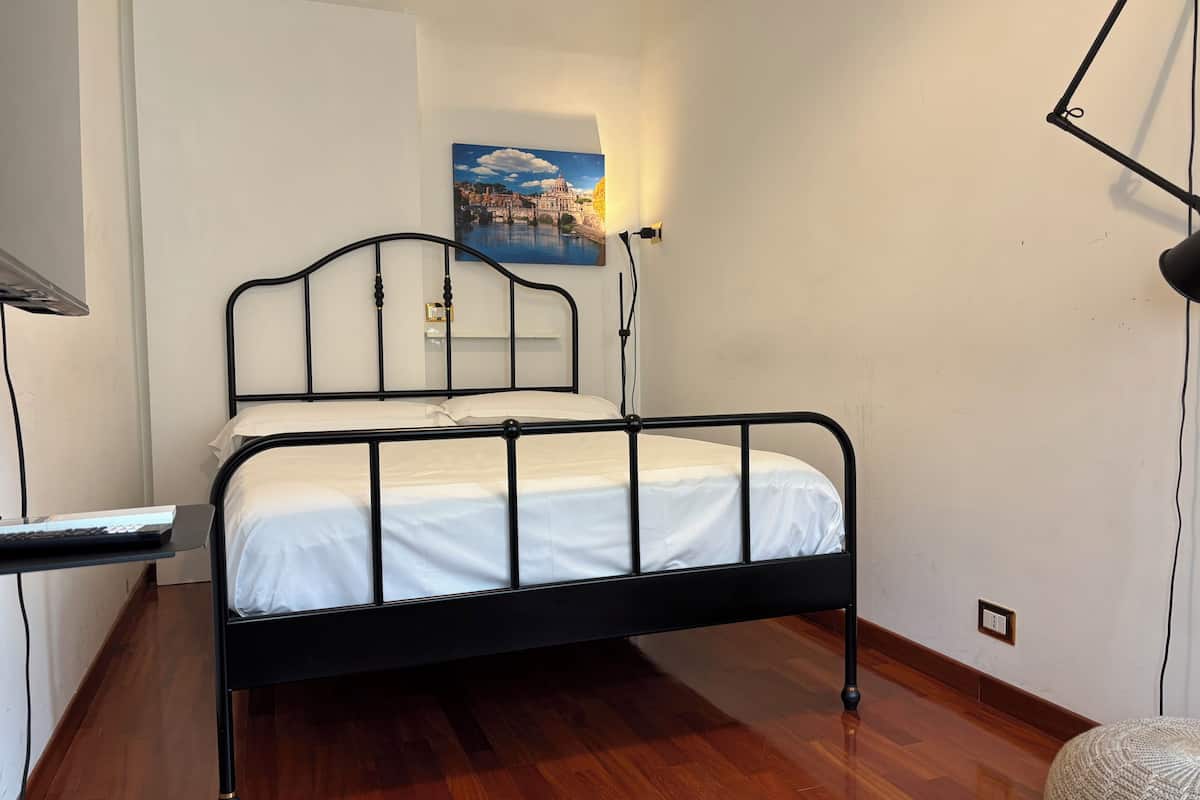 A single bed with a metal frame, a bedside table with a lamp, and a painting on the wall.