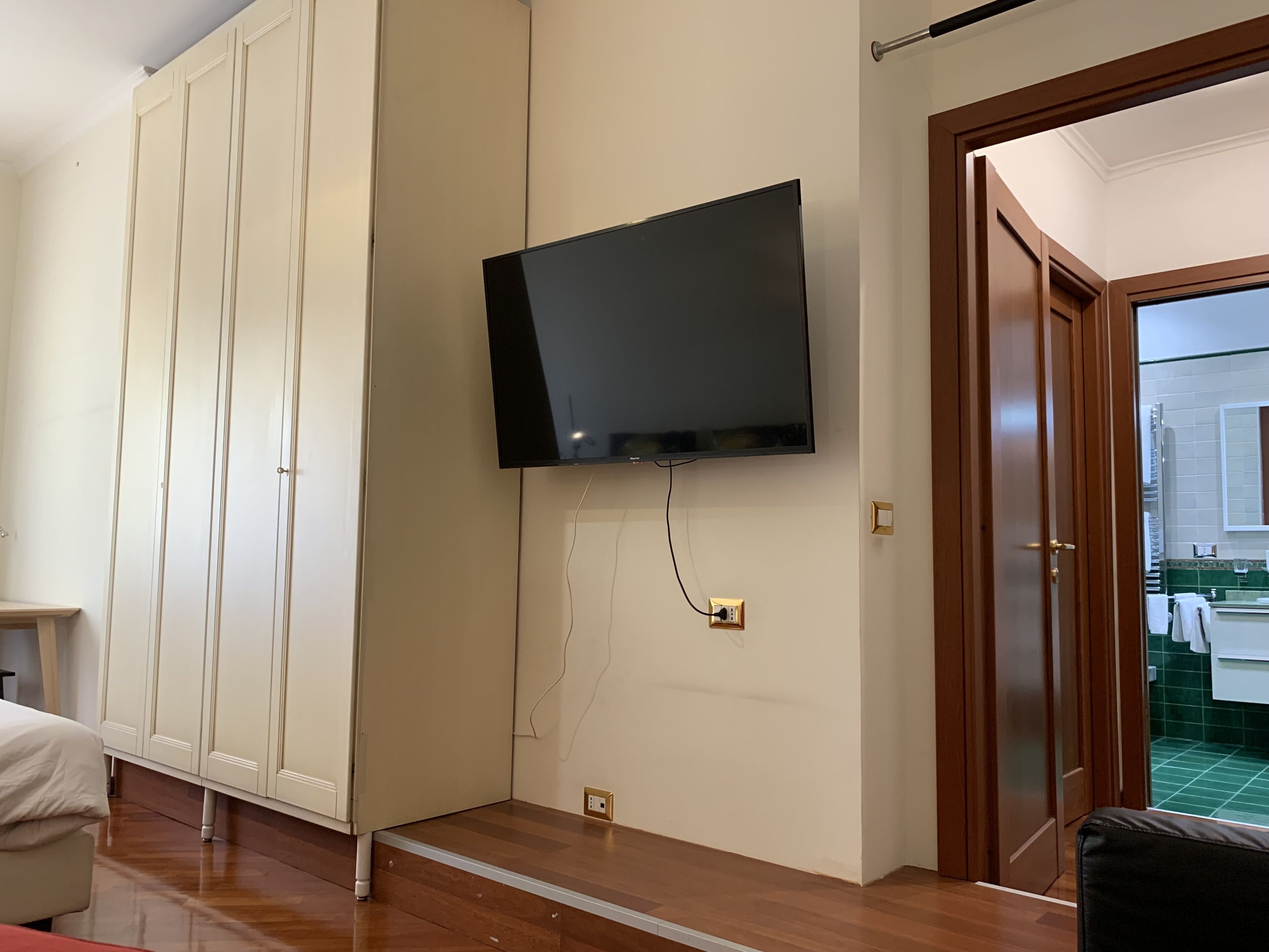 Una habitación con televisión en la pared, una puerta de madera y vistas al exterior.