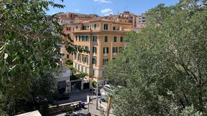 A multi-story building with a yellow facade, surrounded by trees and parked cars. - SmooRoomS Trastevere (Rome)